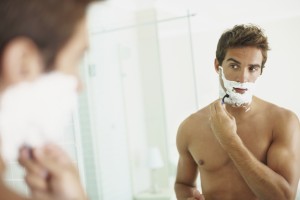 Smart young guy shaving while looking at himself in the mirror